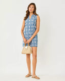 Woman wearing a blue and white checkered dress holding a beige handbag on a white background